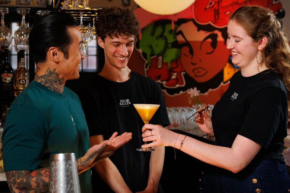 Foodhallen bartenders toast with a tapped cocktail in front of a graffiti wall