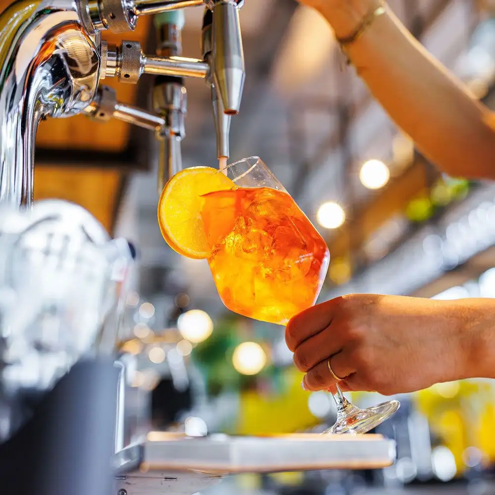 Bartender zapft einen orangefarbenen Cocktail aus einer Springbay Cocktail-Zapfanlage in ein Weinglas