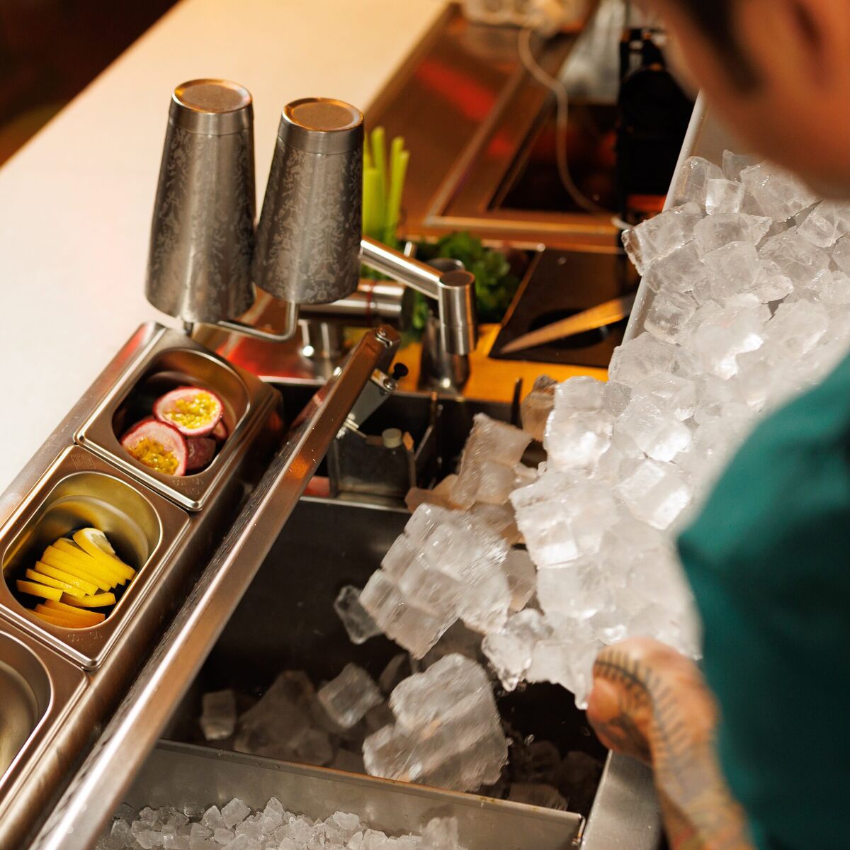 Bartender scooping ice next to the shakers on the station's work surface