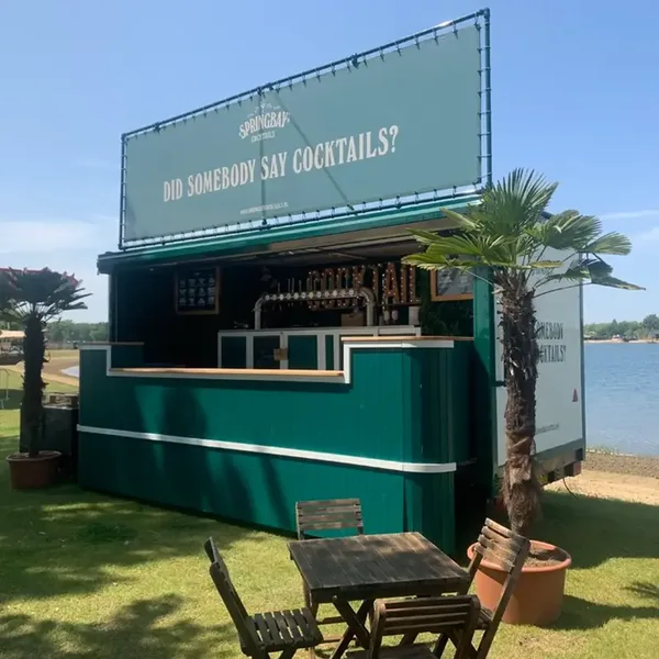 Springbay Cocktail-Trailerbar: acht Meter lange grüne Festivalbar mit offener Klappe, draußen zwischen Palmen