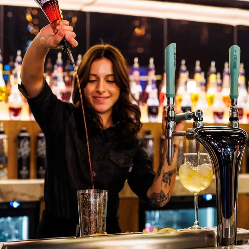 Bartender serviert einen Cocktail an einer Springbay Zapfstation, dahinter eine Wand voller Flaschen